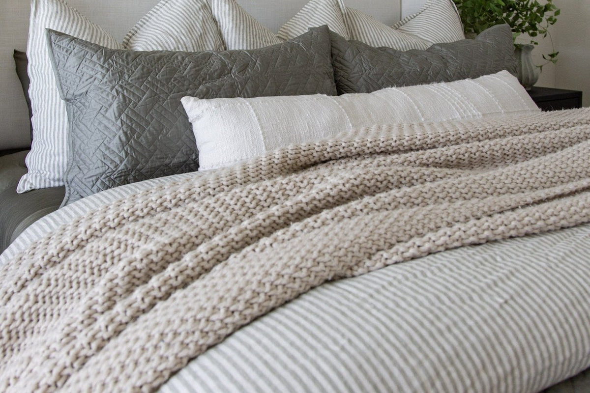 Close view of gray and cream striped bedding with a chunky knit throw and Euro shams