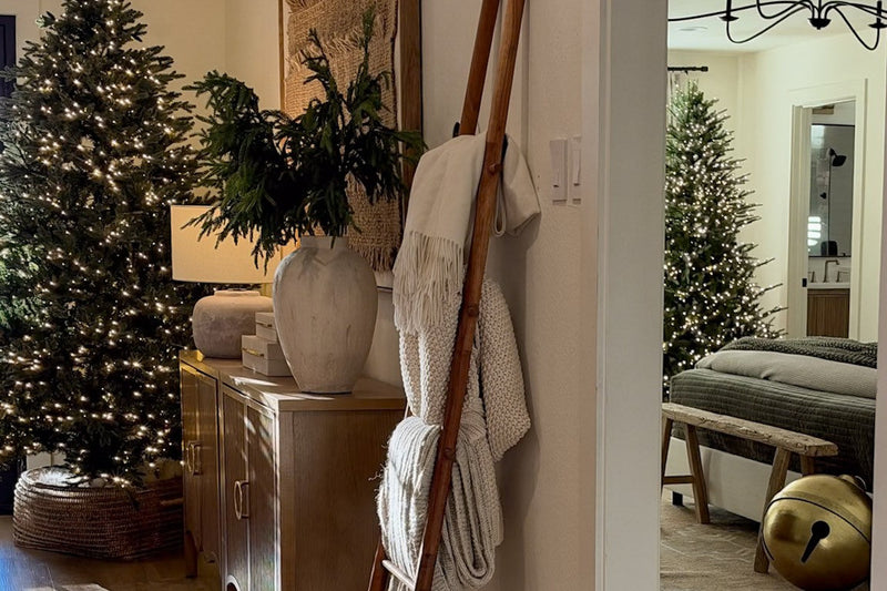 Entry hall dressed for the holidays with a lit Christmas tree in a woven basket, a wood console with greenery in a stone vase, and a wood blanket ladder