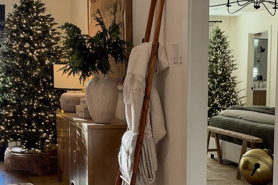 Entry hall dressed for the holidays with a lit Christmas tree in a woven basket, a wood console with greenery in a stone vase, and a wood blanket ladder