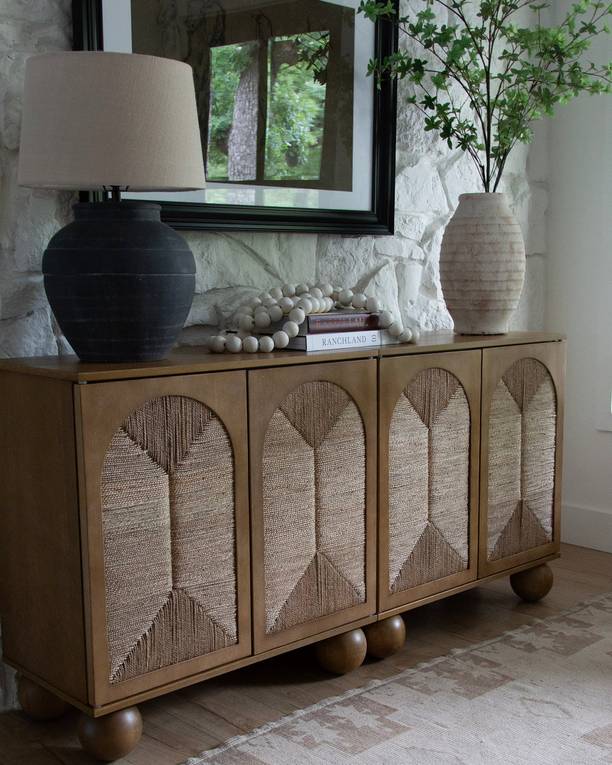 Woven-front sideboard with a black lamp and a vase of branches
